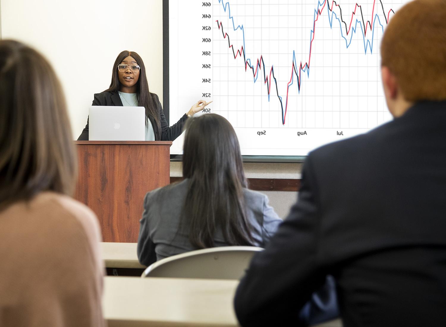 Economics class facing a student presenting at the front of the room.